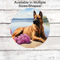 A Belgian Malinois dog surrounded by beautiful flowers on a dock overlooking a lake.