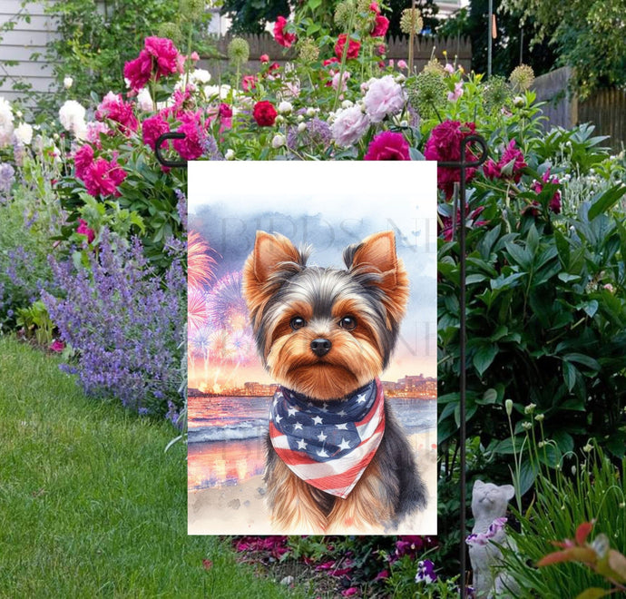 An adorable Yorkshire Terrier Dog wearing an American Flag Bandanna on a Beach with Fireworks in the background.