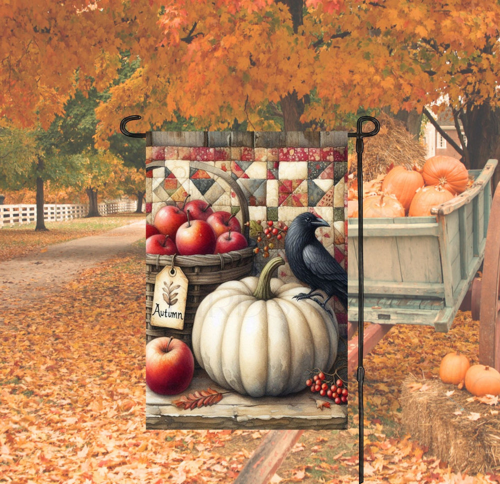 A beautiful primitive Autumn Garden Flag with a basket of apples, a white pumpkin, pip berries and a black Crow against a quilt background.