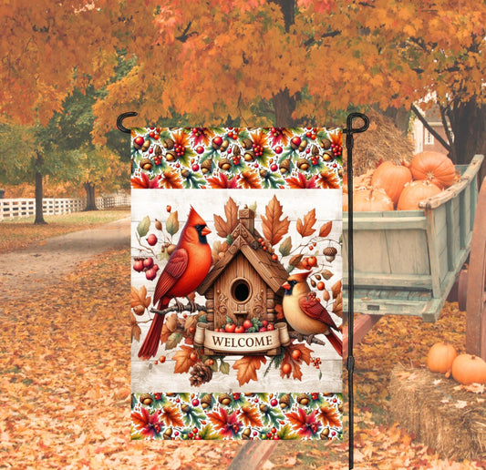 A beautiful Fall Welcome Garden Flag with a Male and Female Cardinal bird on a bird house with Fall leaves and acorns.