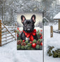 An adorable black French Bulldog in a snowy Winter setting wearing a red bow.