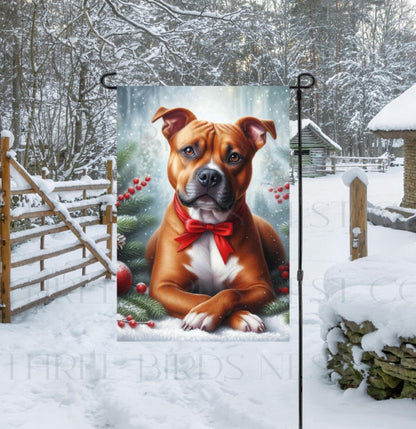 An adorable brown and white Pit Bull dog in a snowy Winter setting wearing a red bow.