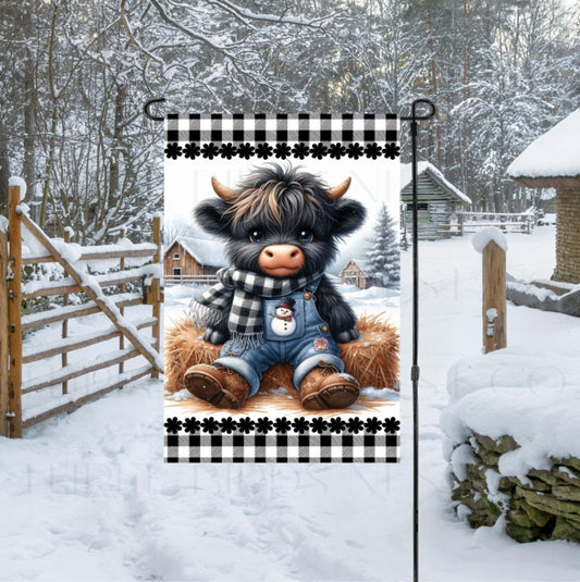 An adorable baby Highland Cow in his overalls with a Snowman