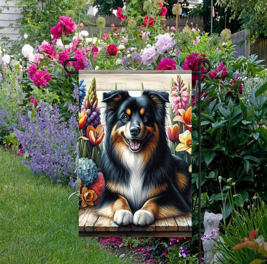 A beautiful black and tan Australian Shepherd dog surrounded by gorgeous flowers.