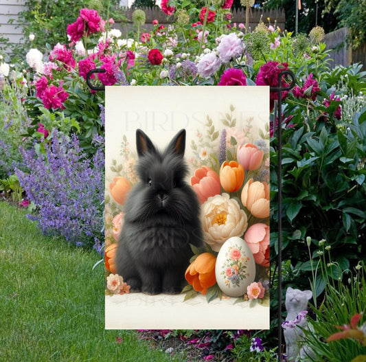 A beautiful black Easter Bunny rabbit with a decorated Easter Egg and surrounded by tulips and peonies.