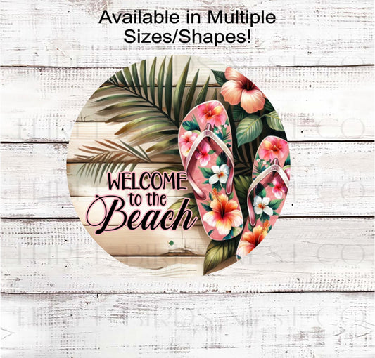 A beautiful Welcome to the Beach sign with palm leaves and hibiscus flowers.