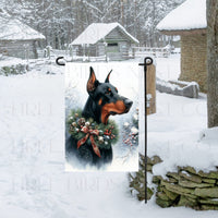 A Black and Rust Colored Doberman Pinscher Dog in a Winter Wonderland setting, wearing a festive collar of greenery and berries with pine cones.