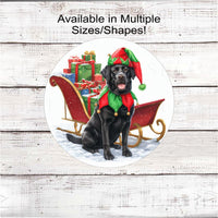 
              A black Labrador Retriever dog dressed as a Christmas Elf next to a sleigh filled with presents
            