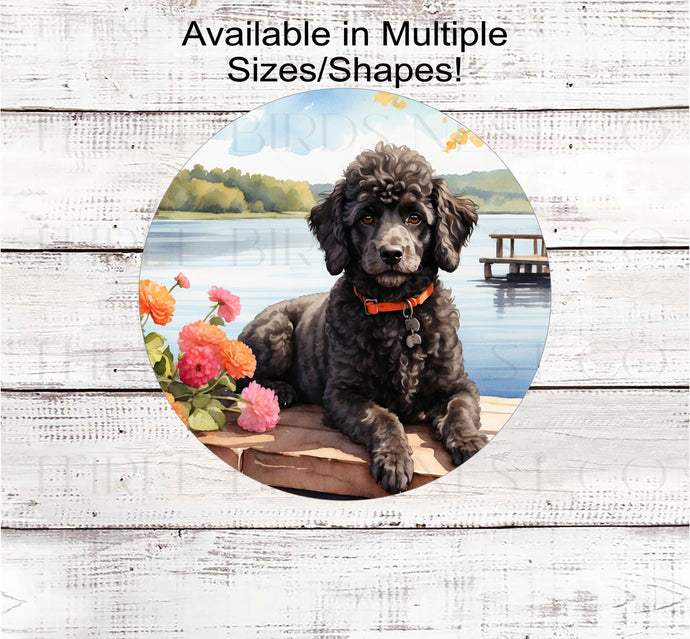 An adorable black Poodle dog with beautiful flowers on a dock overlooking a lake.