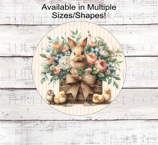 An adorable Easter Bunny in a wood crate surrounded by beautiful flowers and baby chicks.