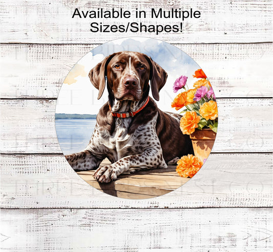 A German Shorthaired Pointer dog surrounded by beautiful Spring flowers on a dock overlooking a lake.